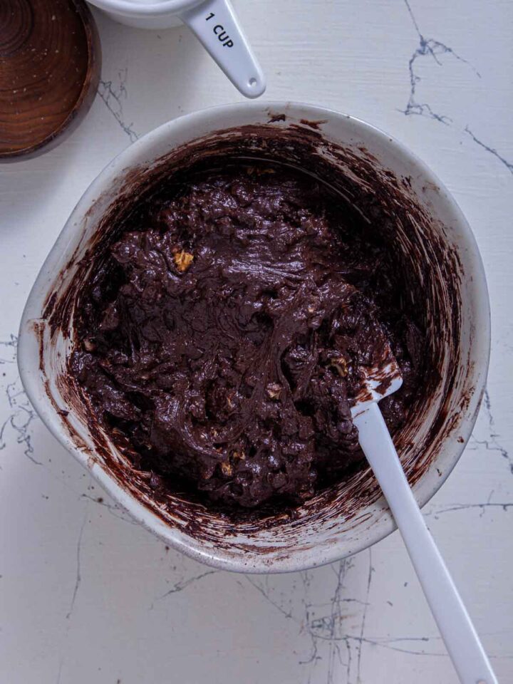 Thick chocolate brownie batter mixed with walnuts in a bowl.