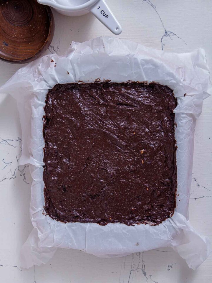 Chocolate brownie batter spread evenly in a parchment-lined baking pan.
