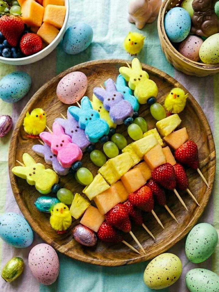 Easter fruit kabobs with strawberries, melon, pineapple, grapes, and colorful Peeps on a wooden platter.