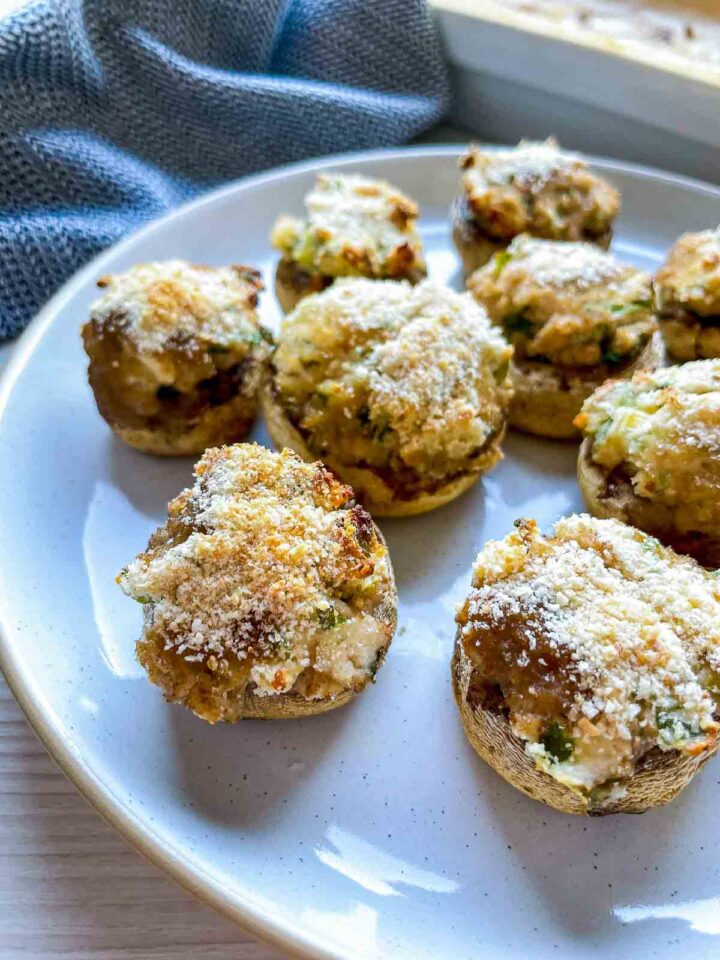 Plate of baked stuffed mushrooms topped with golden herbed cream cheese and grated cheese.