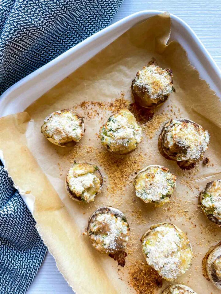 Baked stuffed mushrooms with golden cheese topping on a parchment-lined baking tray.