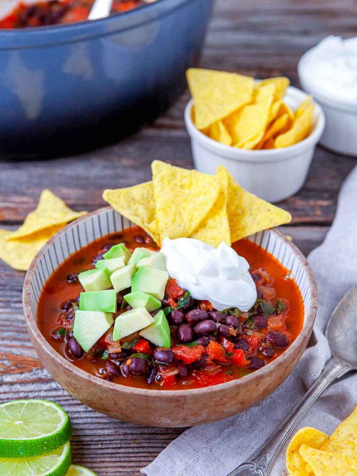 Black bean nacho soup topped with avocado, sour cream, and tortilla chips in a bowl.