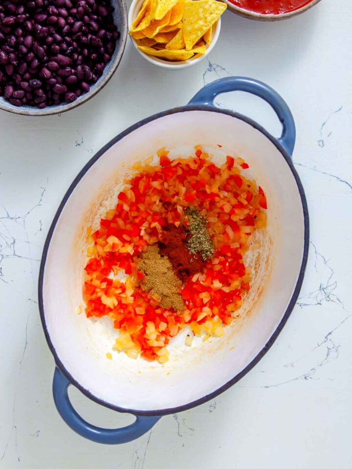 Diced onion and red bell pepper sautéing with spices in a pot for nacho soup.