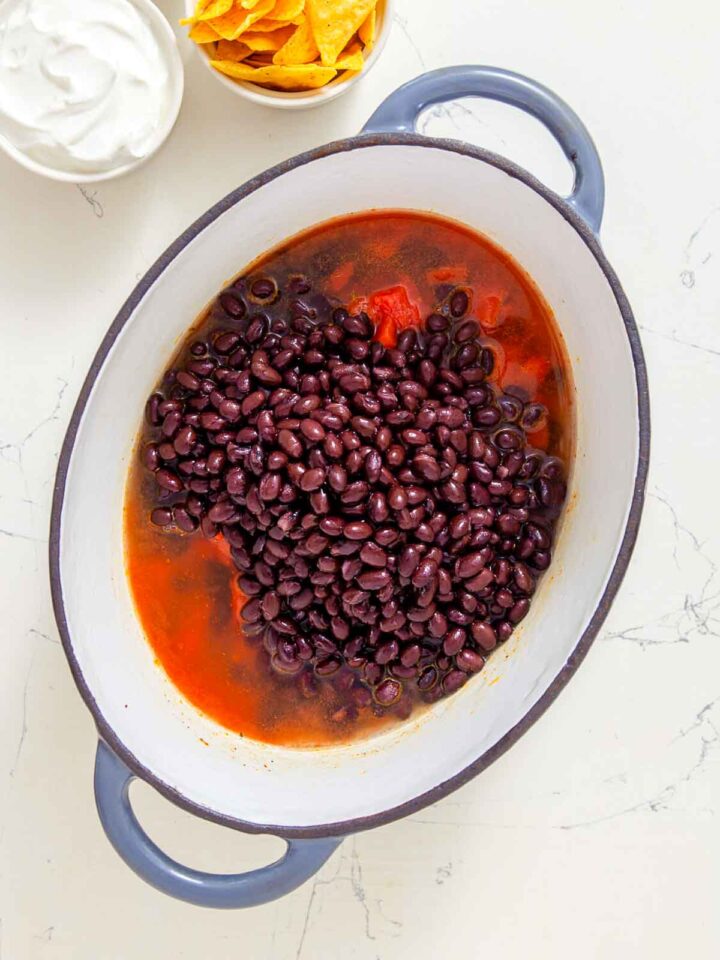 Black beans added to seasoned tomato broth in a pot for nacho soup.