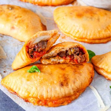 Close-up of sausage-stuffed pizza pocket cut open showing meat, sauce, and cheese filling.
