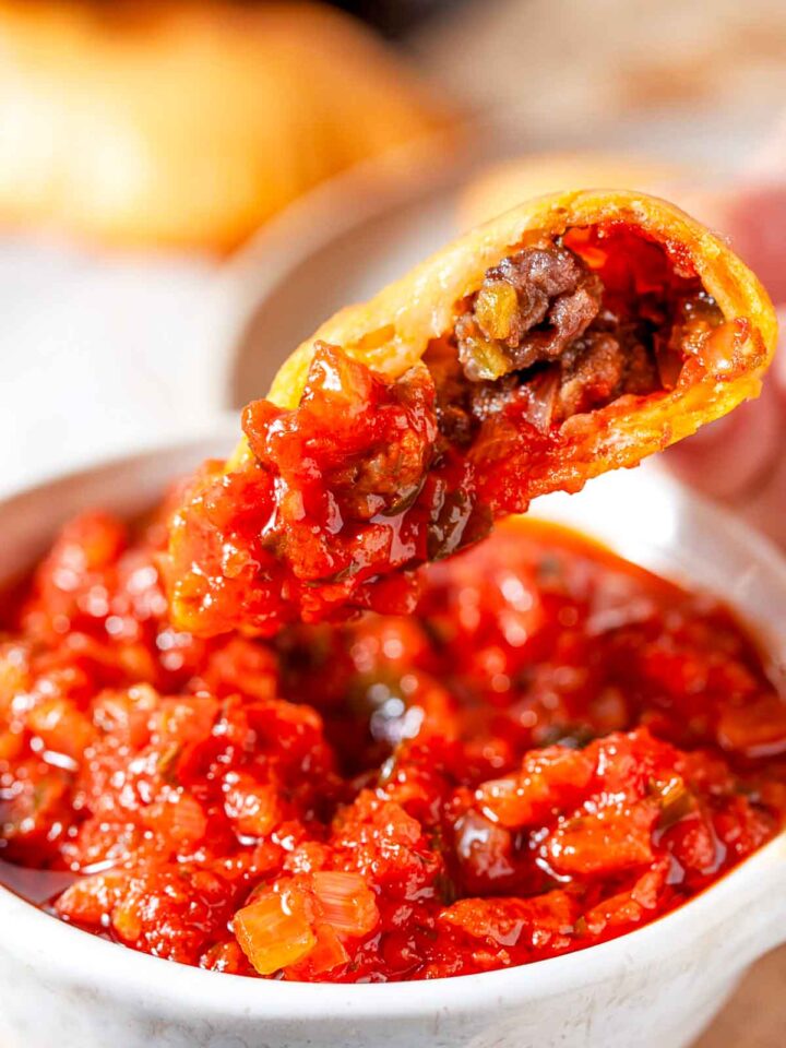 Close-up of sausage pizza pocket dipped in marinara sauce showing meat filling.