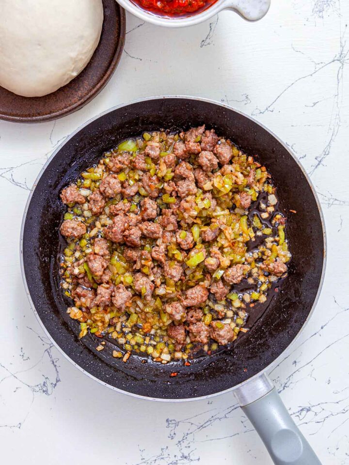 Ground sausage cooking with diced onions and green peppers in a skillet.