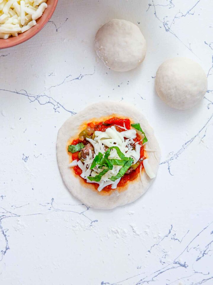 Pizza dough round topped with sausage filling, marinara sauce, cheese, and basil.
