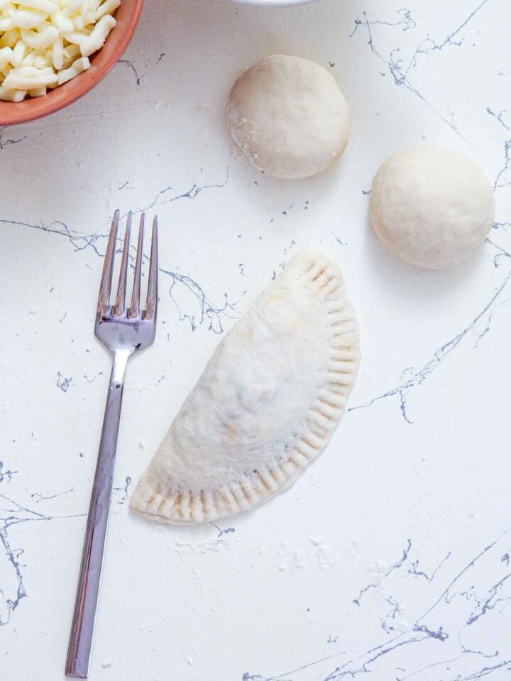 Pizza pocket dough folded and sealed with a fork before baking.