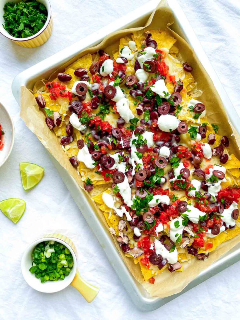 Loaded sheet pan nachos with melted cheese, kidney beans, salsa, sliced olives, sour cream, and chopped green onions.