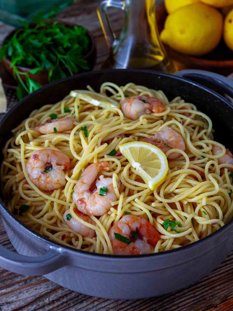 Shrimp scampi pasta with lemon slices and parsley in a skillet.
