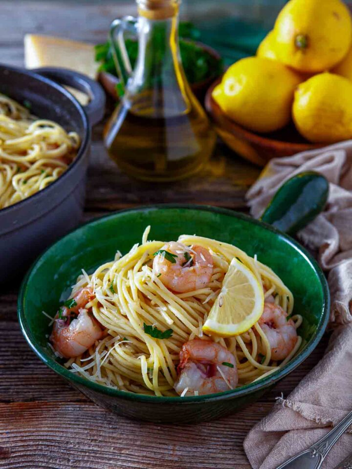 Bowl of shrimp scampi spaghetti with lemon wedge and parsley.