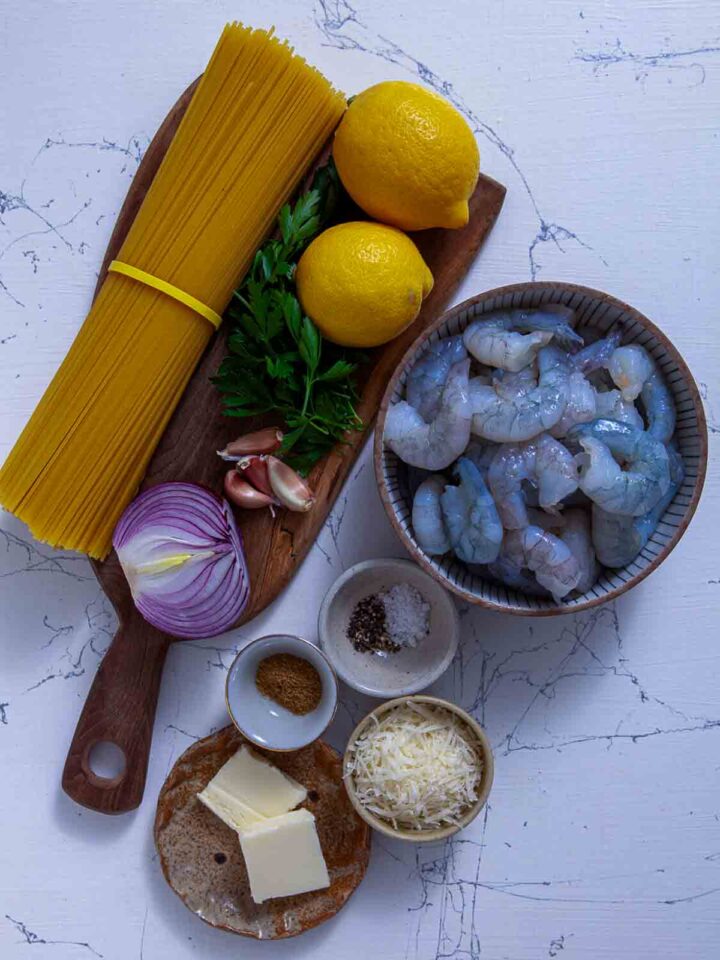 Ingredients for shrimp scampi including shrimp, spaghetti, lemons, garlic, onion, parsley, butter, and cheese.