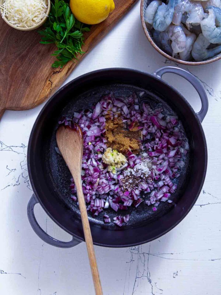 Chopped red onion, garlic, and spices sautéing in a skillet for shrimp scampi.