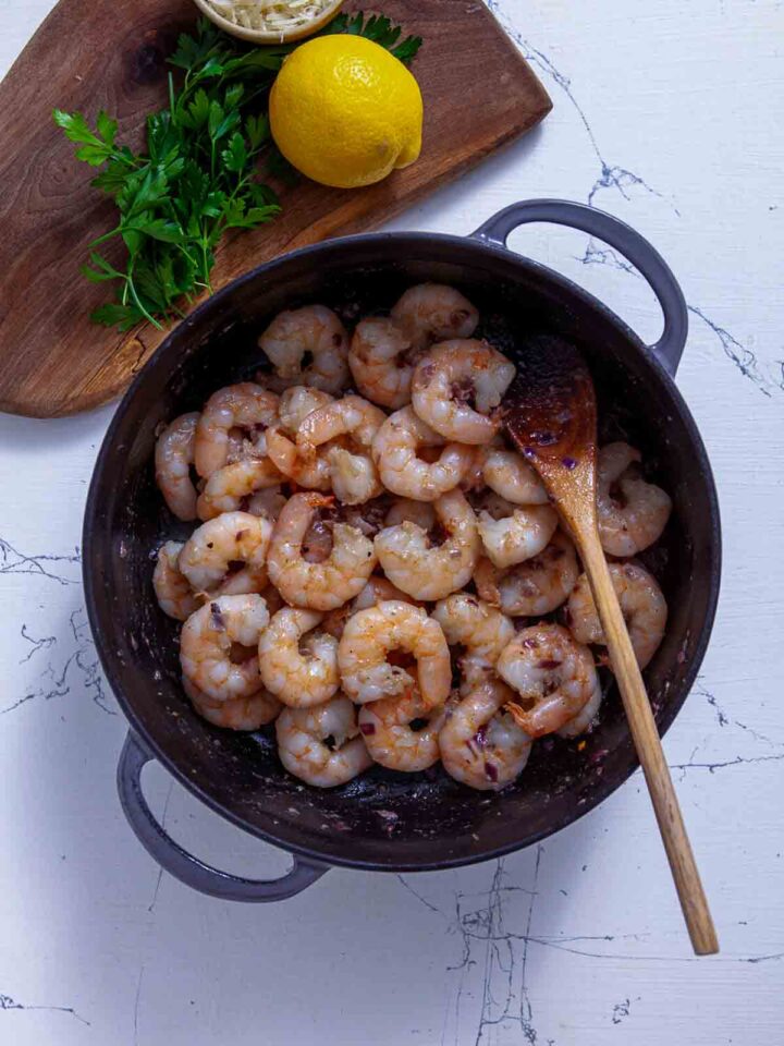 Shrimp sautéing in a skillet with garlic and seasoning for shrimp scampi.