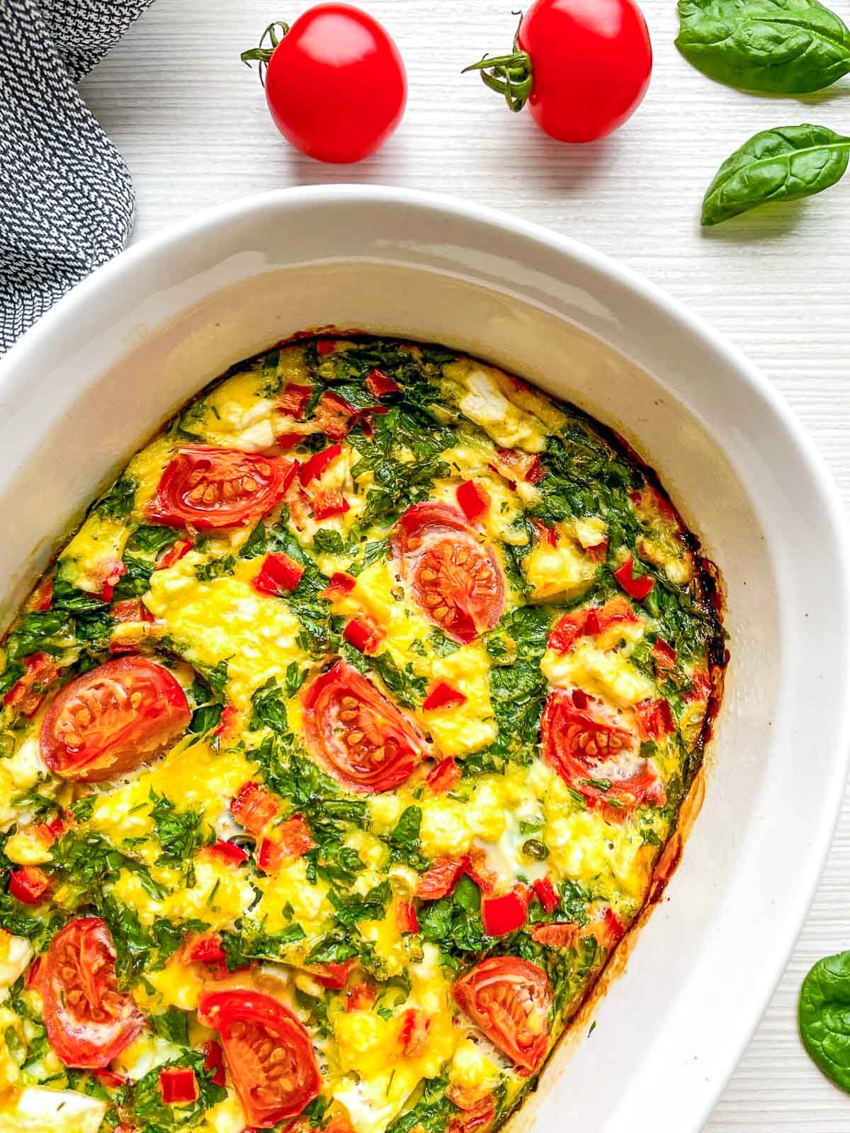 Baked spinach, feta, and tomato breakfast casserole in a white baking dish.
