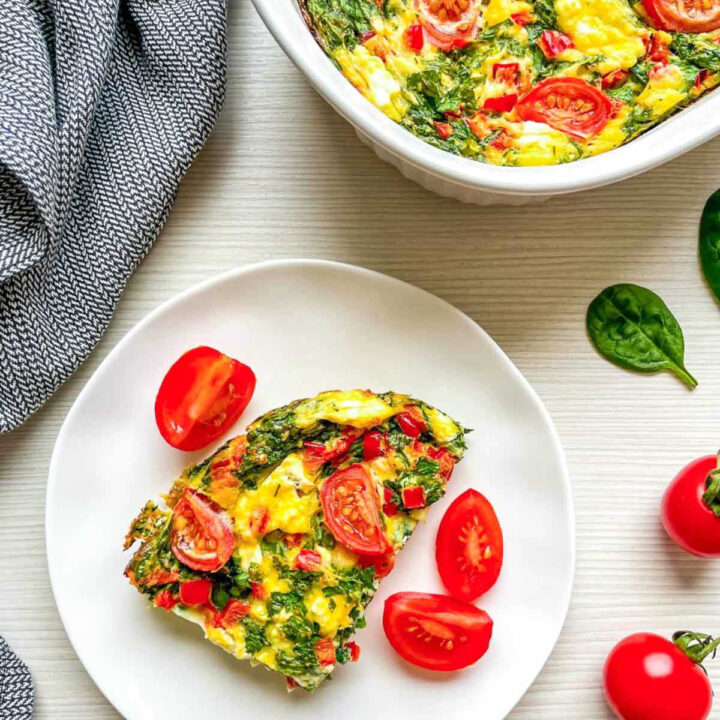 Serving of spinach, feta, and tomato breakfast casserole on a plate with cherry tomatoes.
