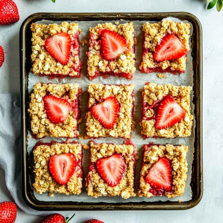 Strawberry rhubarb bars placed on a parchement paper over a baking tray.