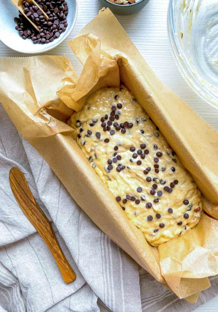 Banana bread batter poured into a parchment-lined loaf pan, topped with chocolate chips, ready to bake into a moist almond chocolate banana bread.