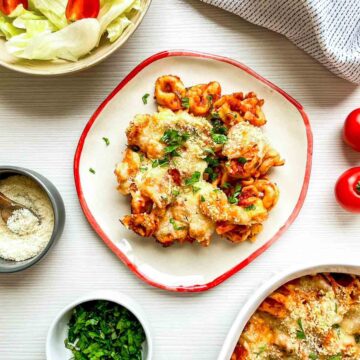 Golden, cheesy baked tortellini garnished with fresh herbs, served with a crisp salad and parmesan on a bright, minimal table setting.