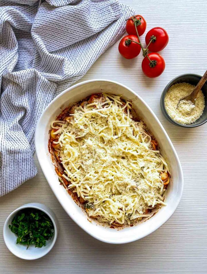 Tortellini layered with marinara sauce and topped generously with shredded cheese and parmesan, ready to be baked.