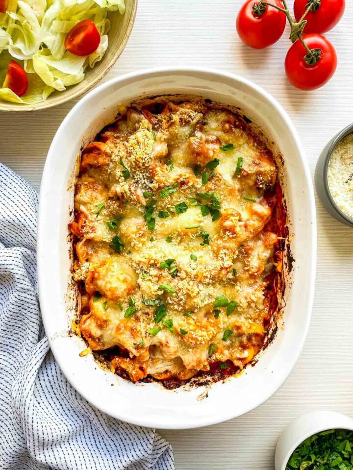 Baked tortellini finished with melted golden cheese, sprinkled parmesan, and fresh herbs, ready to serve.