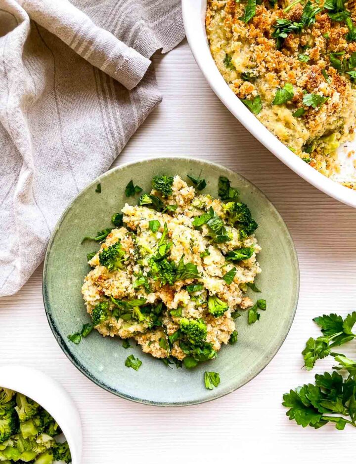 A warm serving of broccoli cheddar quinoa gratin, scooped onto a plate with crispy topping, tender broccoli, and fresh herbs for a wholesome, comforting bite.