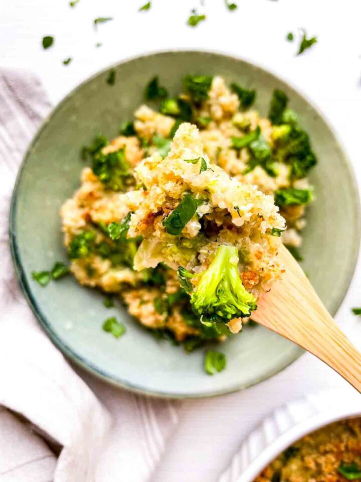 Broccoli au gratin scooped on a spoon and held over the plate.