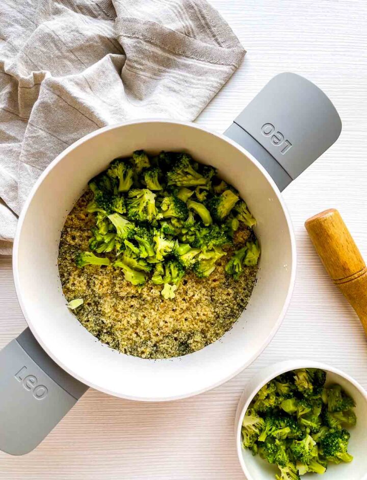 Tender cooked quinoa topped with vibrant broccoli florets, ready to be mixed into a hearty, cheesy gratin.