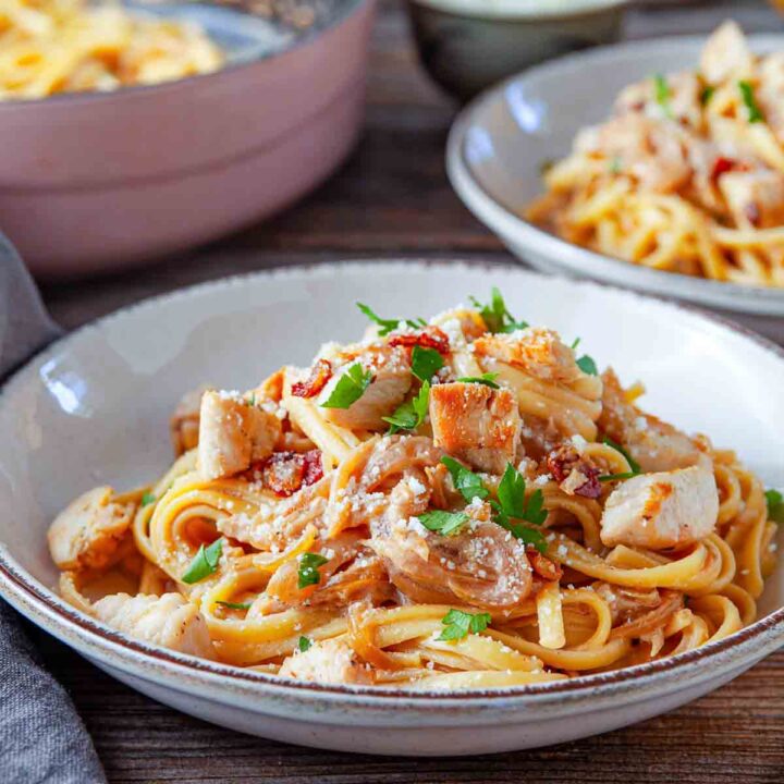 The finished pasta is plated and topped with chicken, herbs, and cheese for serving.