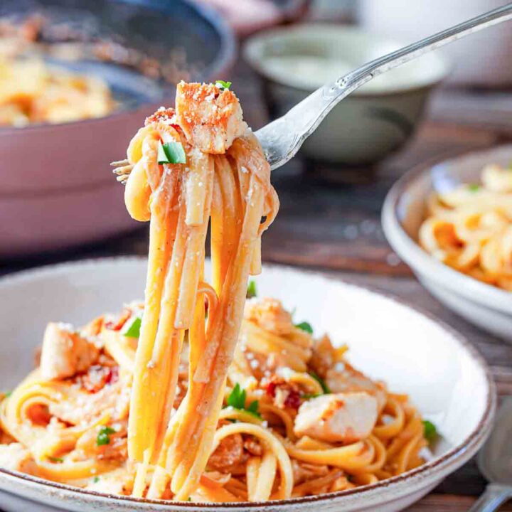 Linguine and chicken on a fork held over a bowl of served pasta.