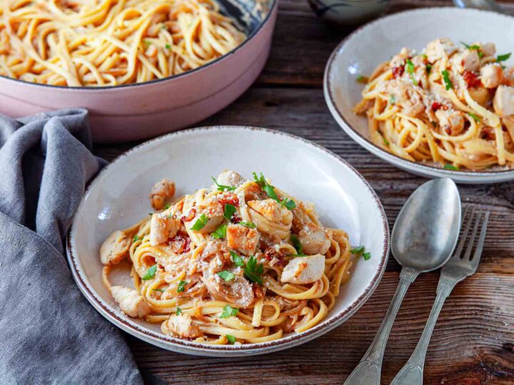 Two served plates of caramelized onion and chicken linguine with the skillet in the background.