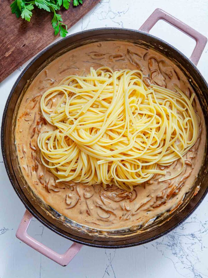 Cooked pasta is added to the creamy sauce, ready to be tossed and coated evenly.