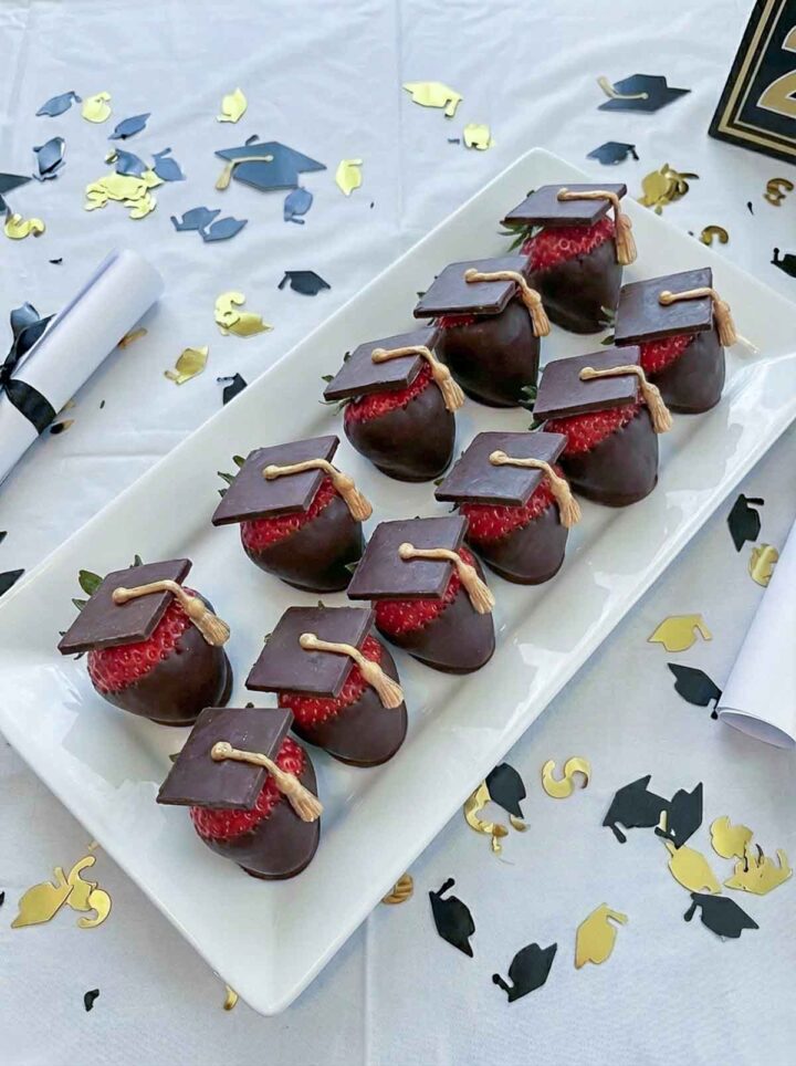 A plate of strawberries dipped in chocolate and decorated with a graduation hat.