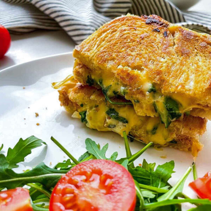 Close-up of grilled cheese sandwich with melted cheese, greens, and tomato slices
