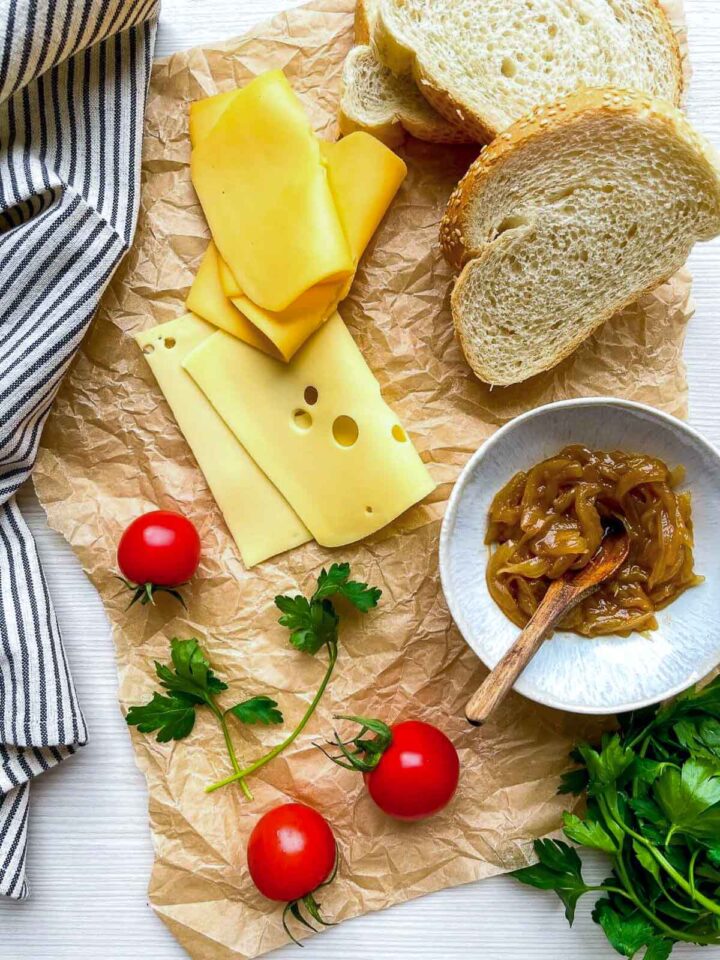 Sliced cheese, bread, caramelized onions, and cherry tomatoes on parchment