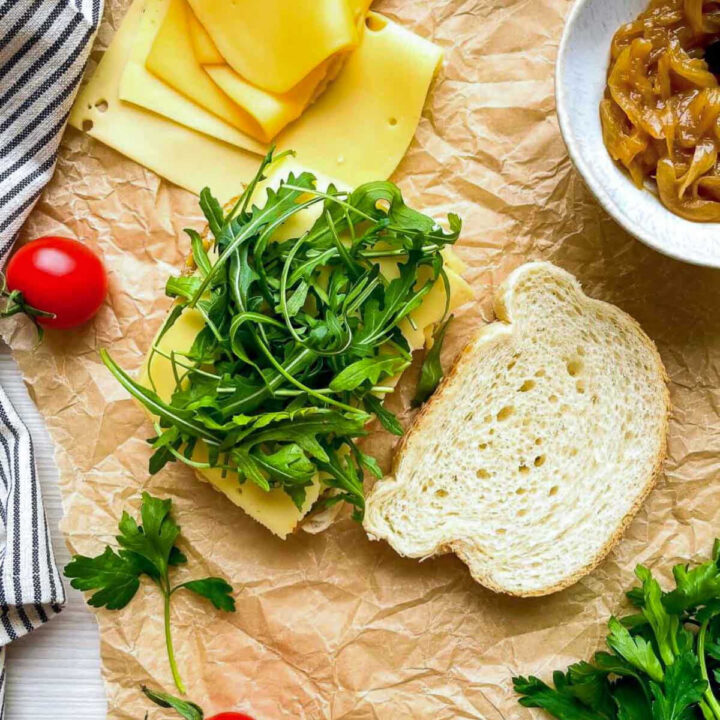 Bread with cheese and arugula being assembled on parchment
