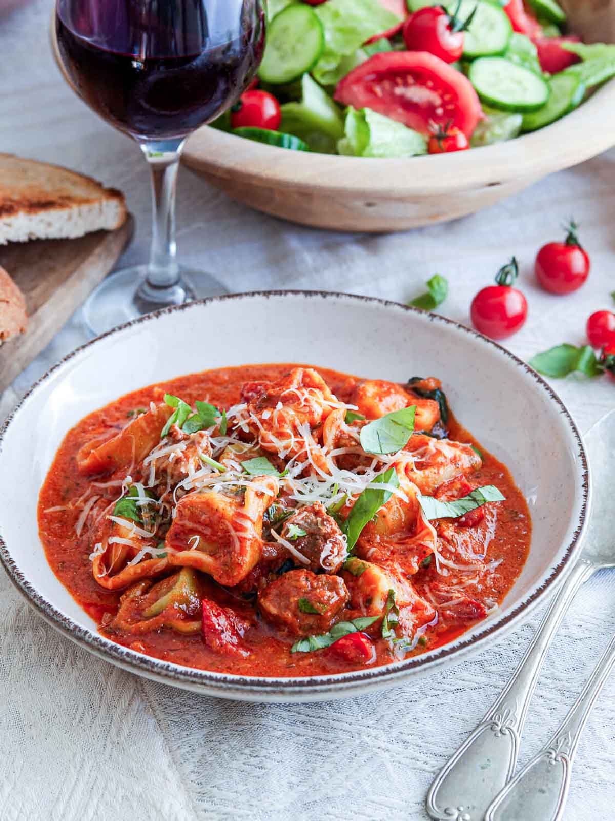 Italian sausage tortellini in tomato sauce with basil, parmesan, salad, and red wine