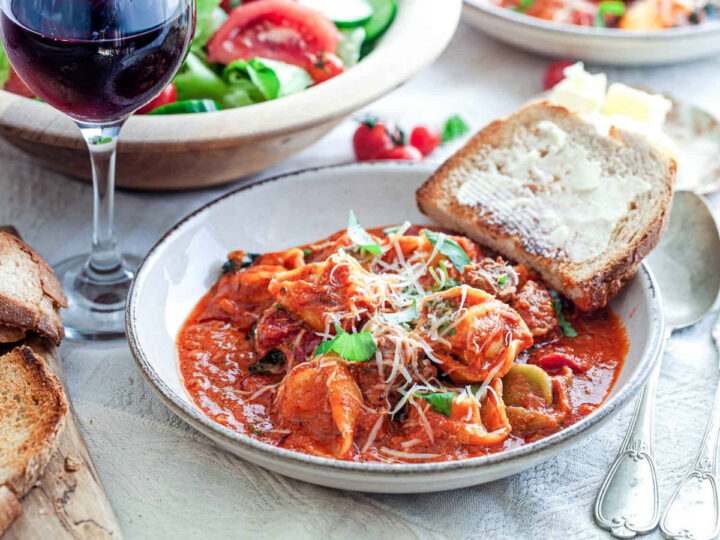 Close up of Italian sausage tortellini in tomato sauce with basil, parmesan, salad, and red wine.