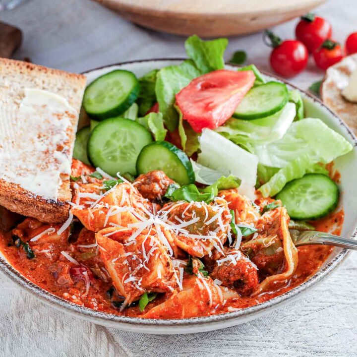 Close up of tortellini in tomato sauce with sausage, basil, and buttered toast