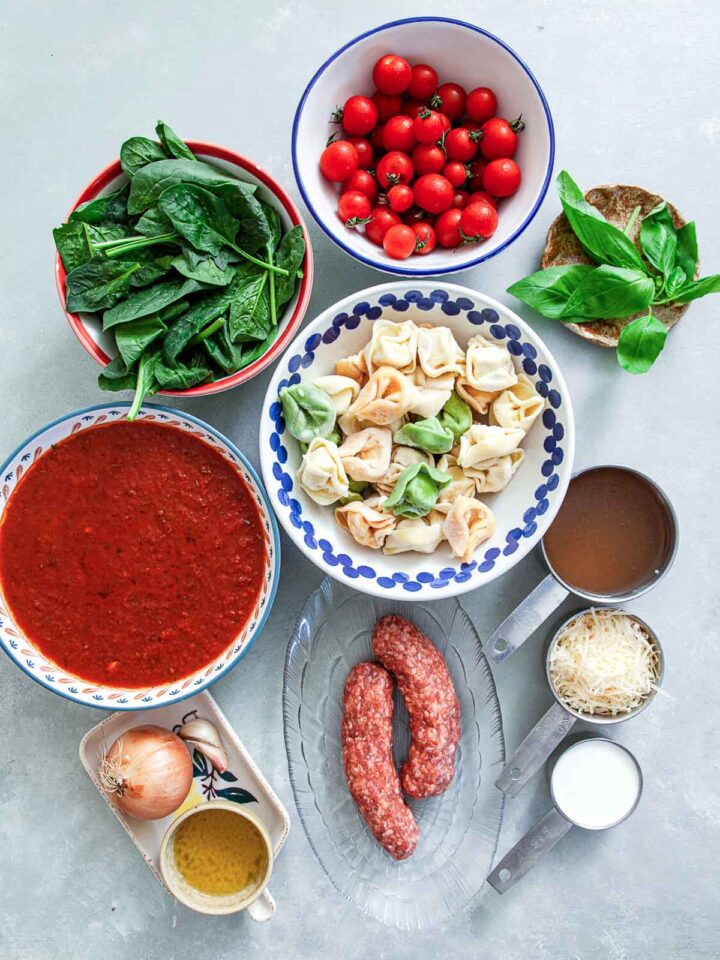 Ingredients for sausage tortellini: pasta, spinach, tomatoes, sauce, sausage, cheese, and broth