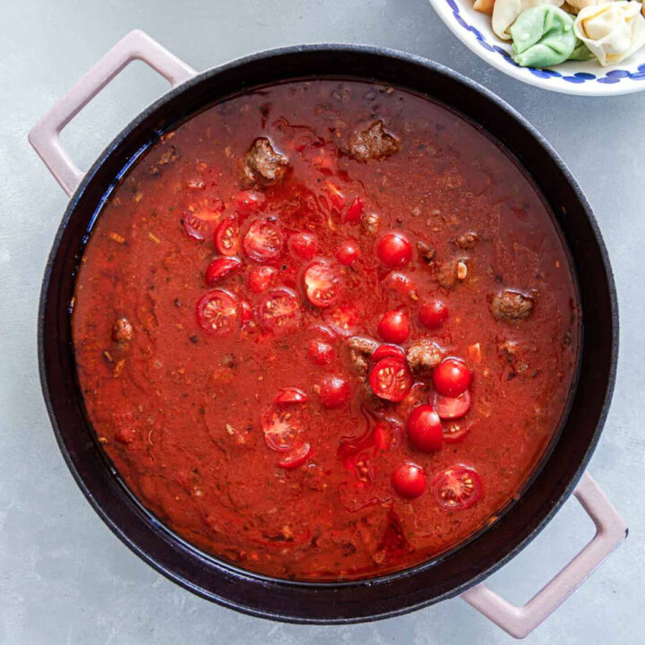 Tomato sauce with sausage and cherry tomatoes simmering in a skillet