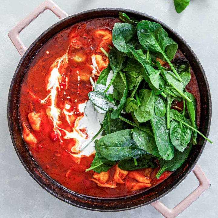 Heavy cream swirled into the tomato tortellini skillet with a large pile of fresh baby spinach added on one side.