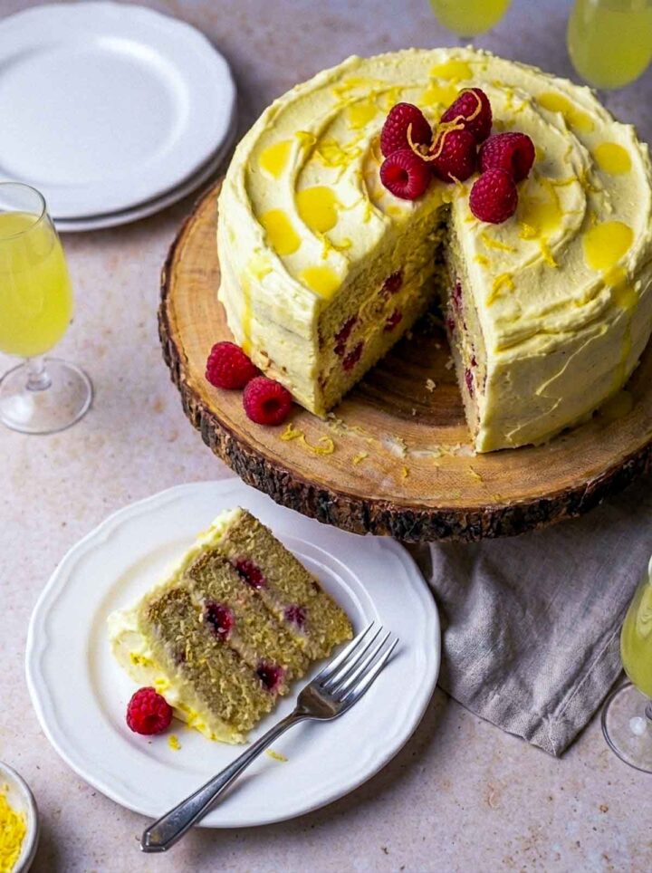 Limoncello raspberry layer cake with creamy lemon frosting and lemon drizzle, topped with fresh raspberries and served with a slice on a plate.