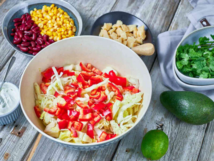 Chopped cabbage and red peppers are mixed in a bowl as the base for a fresh, colorful salad.