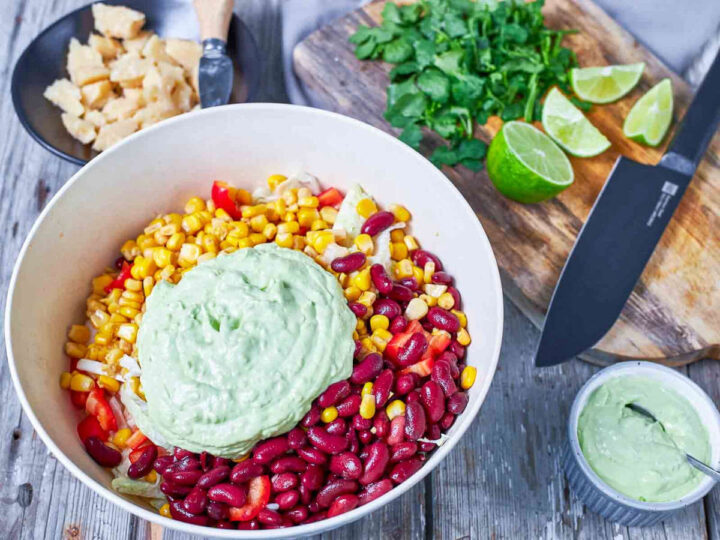 Beans, corn, and vegetables are combined in a bowl and topped with a creamy avocado dressing.