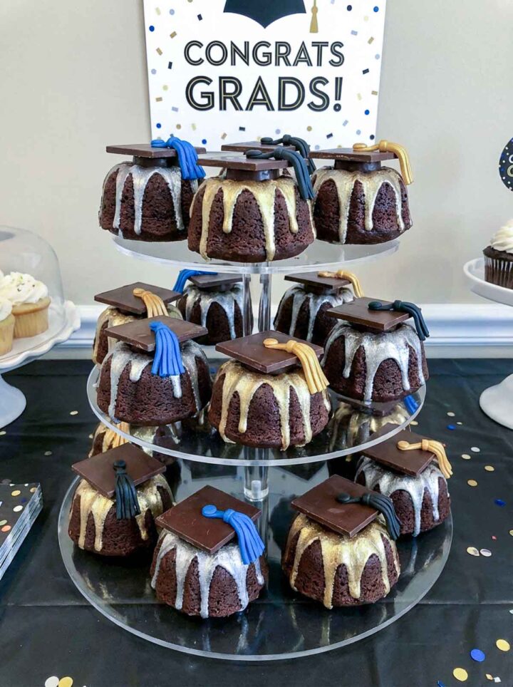 A stack of mini bundt cakes placed on a cake stand and decorated for a graduation party.