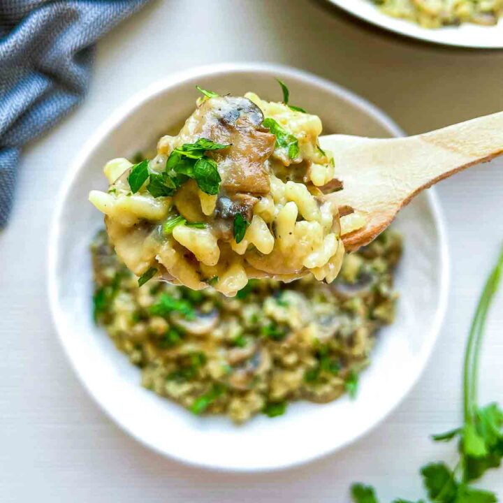 Wooden spoon lifting a scoop of mushroom herb rice from a white bowl showing the silky texture.