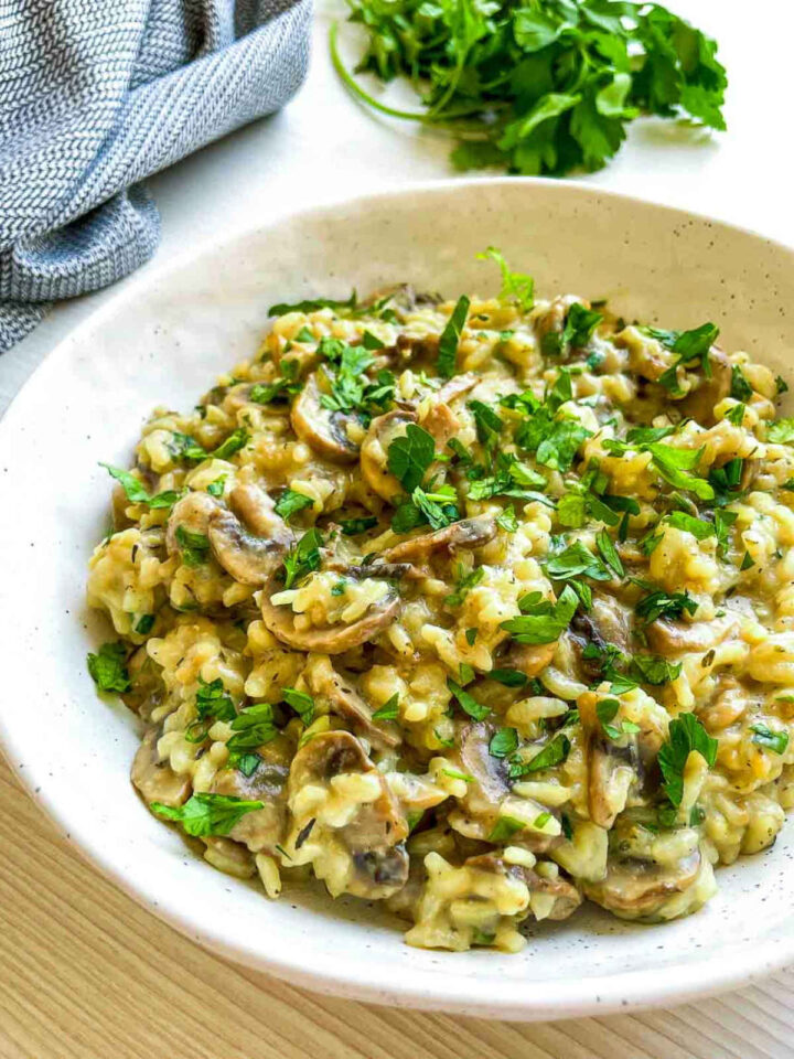 Close-up of mushroom herb rice in a white speckled bowl topped with chopped fresh parsley.