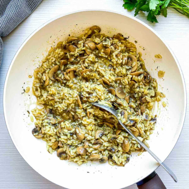 Creamy mushroom rice cooking in pan with spoon.